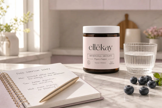 Ellekay Morning Skinny supplement bottle beside an open bloating diary journal on a marble kitchen counter in warm morning light