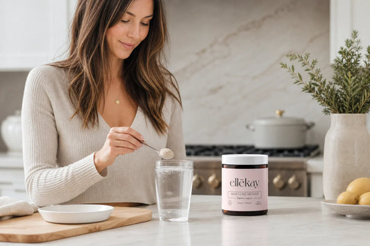 A woman preparing a morning wellness drink in a bright airy kitchen with fresh herbs, a glass of water, and sliced lemon on a marble counter, representing gut health and immune support