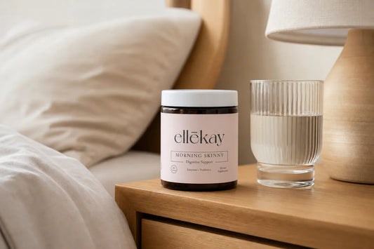 A woman resting peacefully in soft morning light with a glass of water and a digestive wellness supplement on her nightstand, warm neutral tones